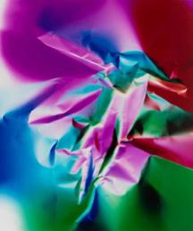A photograph with muted gray colors shows a stone quarry from high up, looking down at the floor and three sides of a roughly rectangular space. Stone has been removed from the quarry walls in horizontal rows, and combined with the muted gray of the rock it gives the impression of high-rise apartments. Far below at the floor of the quarry, the bright orange of heavy machinery offers spots of color.