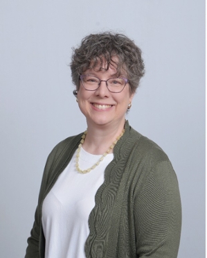 Jean Graves, a light-skinned person with short, grayish hair, glasses, and a wide smile, looks directly out at the viewer.