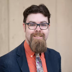 A man with short brown hair and a medium-length goatee and rectangular glasses smiles out at the camera.