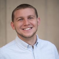 A young person with close-cropped hair and a slight beard smiles out at the camera.