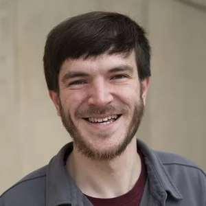 A man with dark hair and a short beard smiles widely out at the camera.